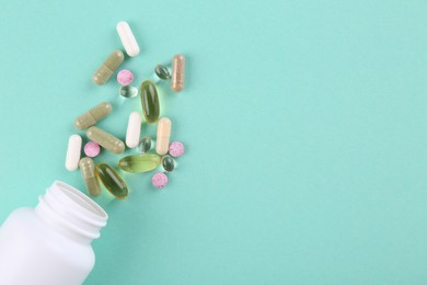 Photo of Bottle and different vitamin pills on turquoise background, top view. Space for text