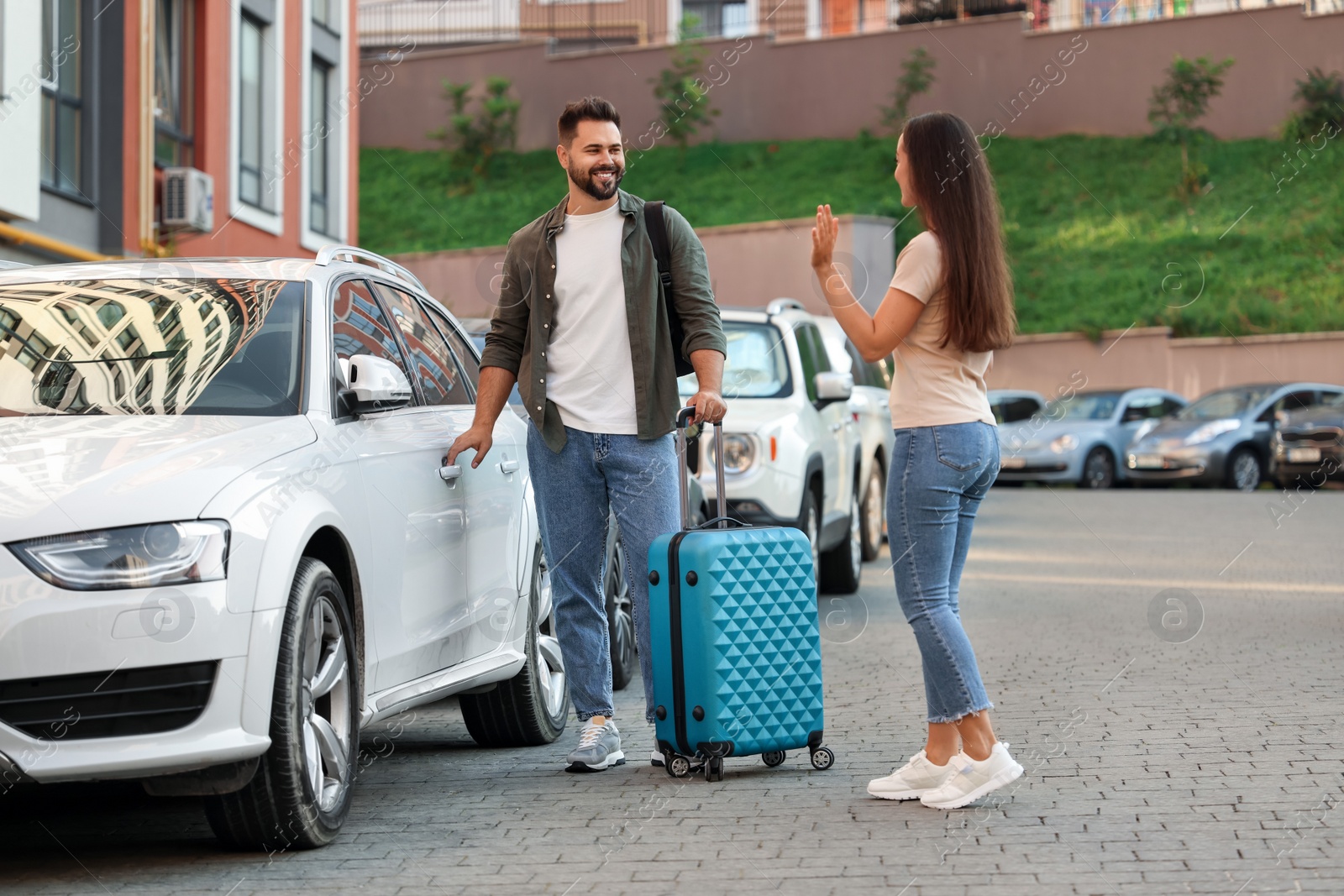 Photo of Long-distance relationship. Woman waving to her boyfriend with luggage near car outdoors