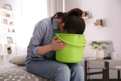 Photo of Young woman with bucket suffering from nausea at home. Food poisoning