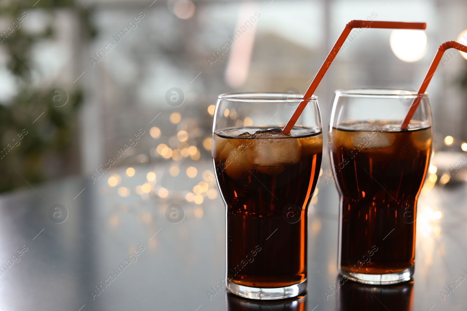 Photo of Glasses of cold cola against blurred fairy lights. Space for text