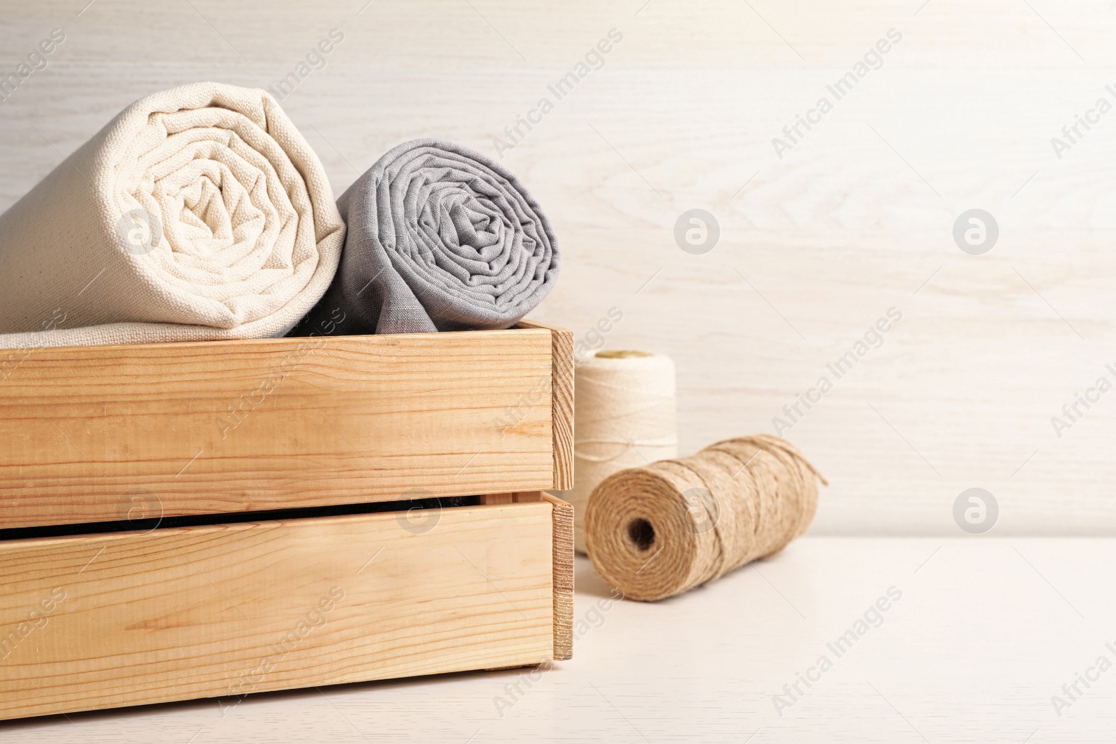 Photo of Hemp cloths in crate and threads on white wooden table, space for text
