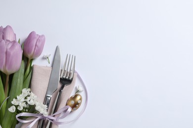 Cutlery set, Easter egg and beautiful flowers on white background, flat lay with space for text. Festive table setting