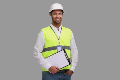 Engineer in hard hat holding clipboard on grey background