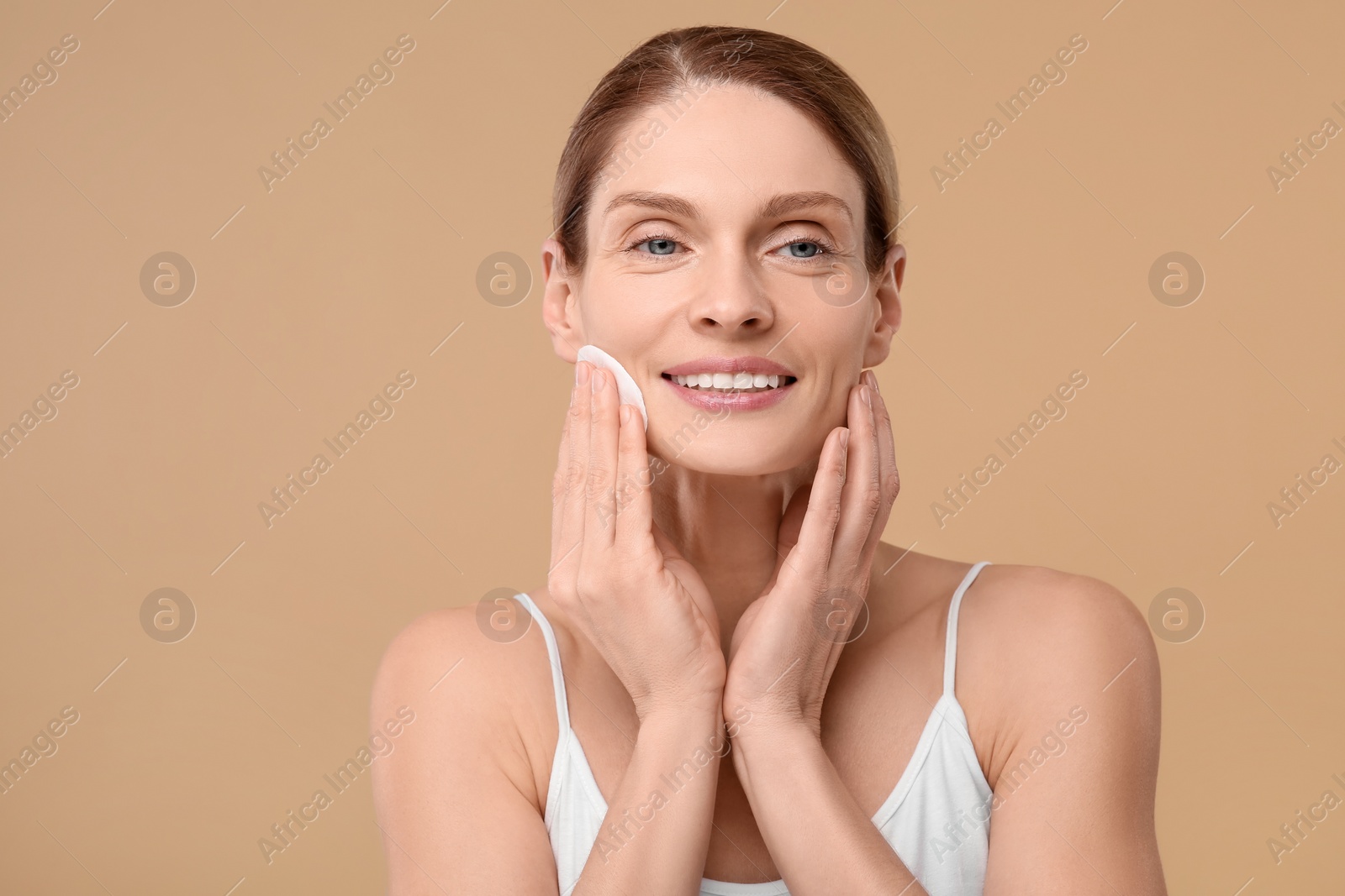 Photo of Beautiful woman removing makeup with cotton pad on beige background