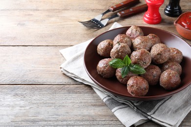 Photo of Tasty cooked meatballs with basil served on wooden table. Space for text