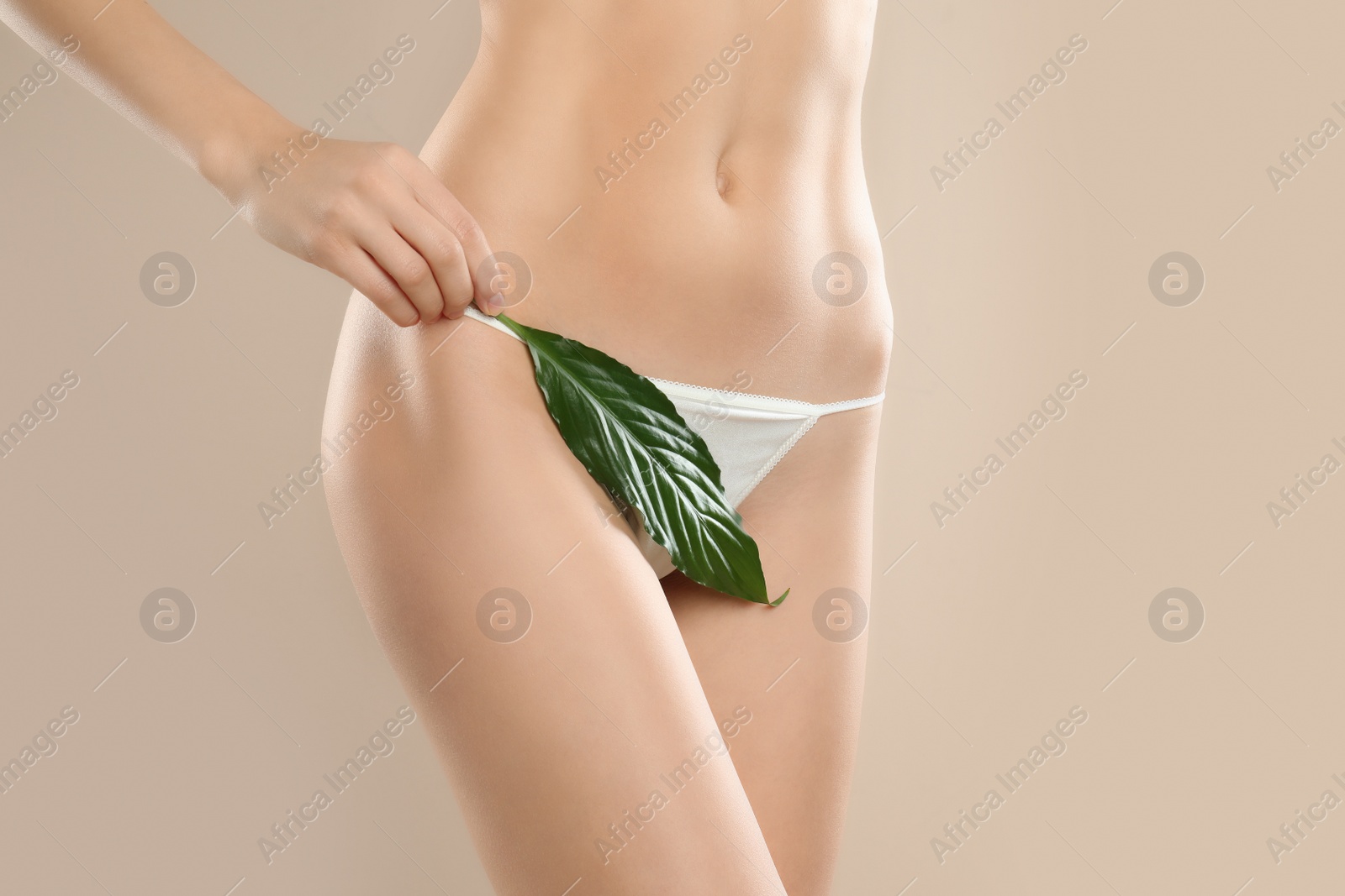 Photo of Woman with leaf showing smooth skin after Brazilian bikini epilation on beige background, closeup. Body care concept