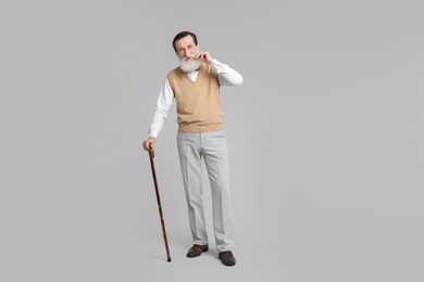 Senior man with walking cane on light gray background