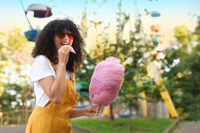Happy woman eating cotton candy at funfair. Space for text