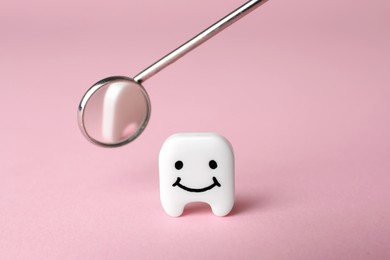 Photo of Decorative tooth with funny face and dentist mirror on pink background, closeup