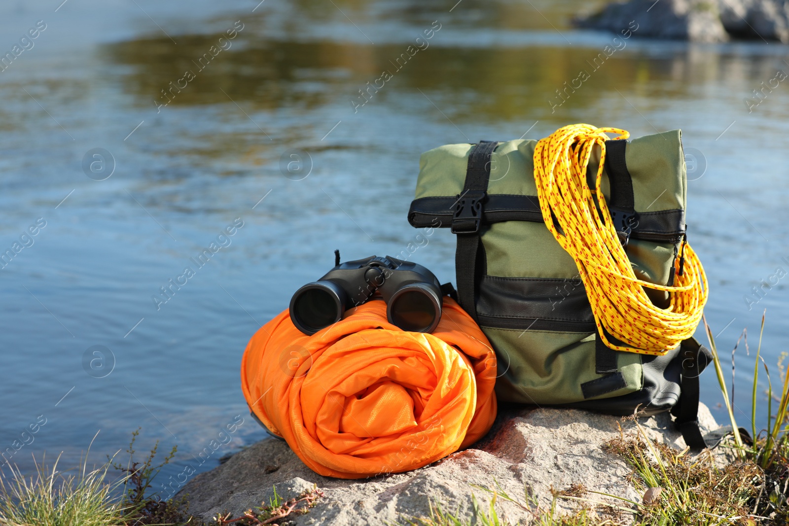 Photo of Set of camping equipment with sleeping bag on rock outdoors. Space for text