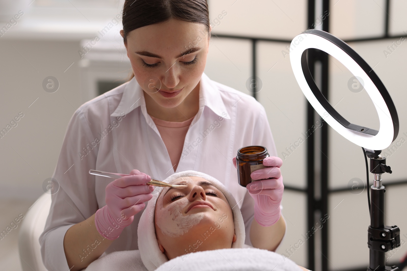 Photo of Cosmetologist applying mask on woman's face in clinic