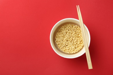 Cup of instant noodles with chopsticks on color background, top view. Space for text