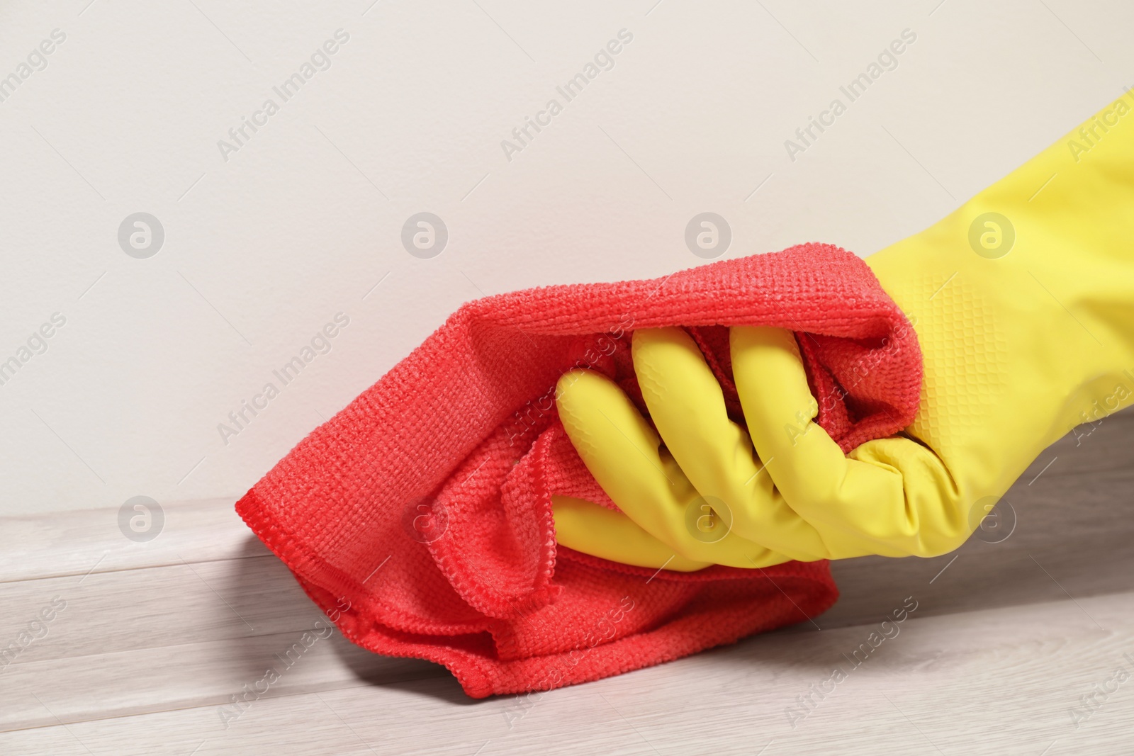 Photo of Woman in gloves cleaning plinth with cloth indoors, closeup