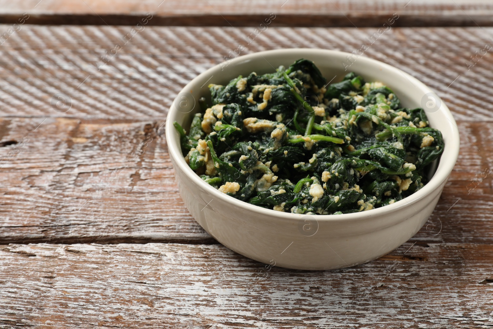 Photo of Tasty spinach dip with eggs in bowl on wooden table, space for text