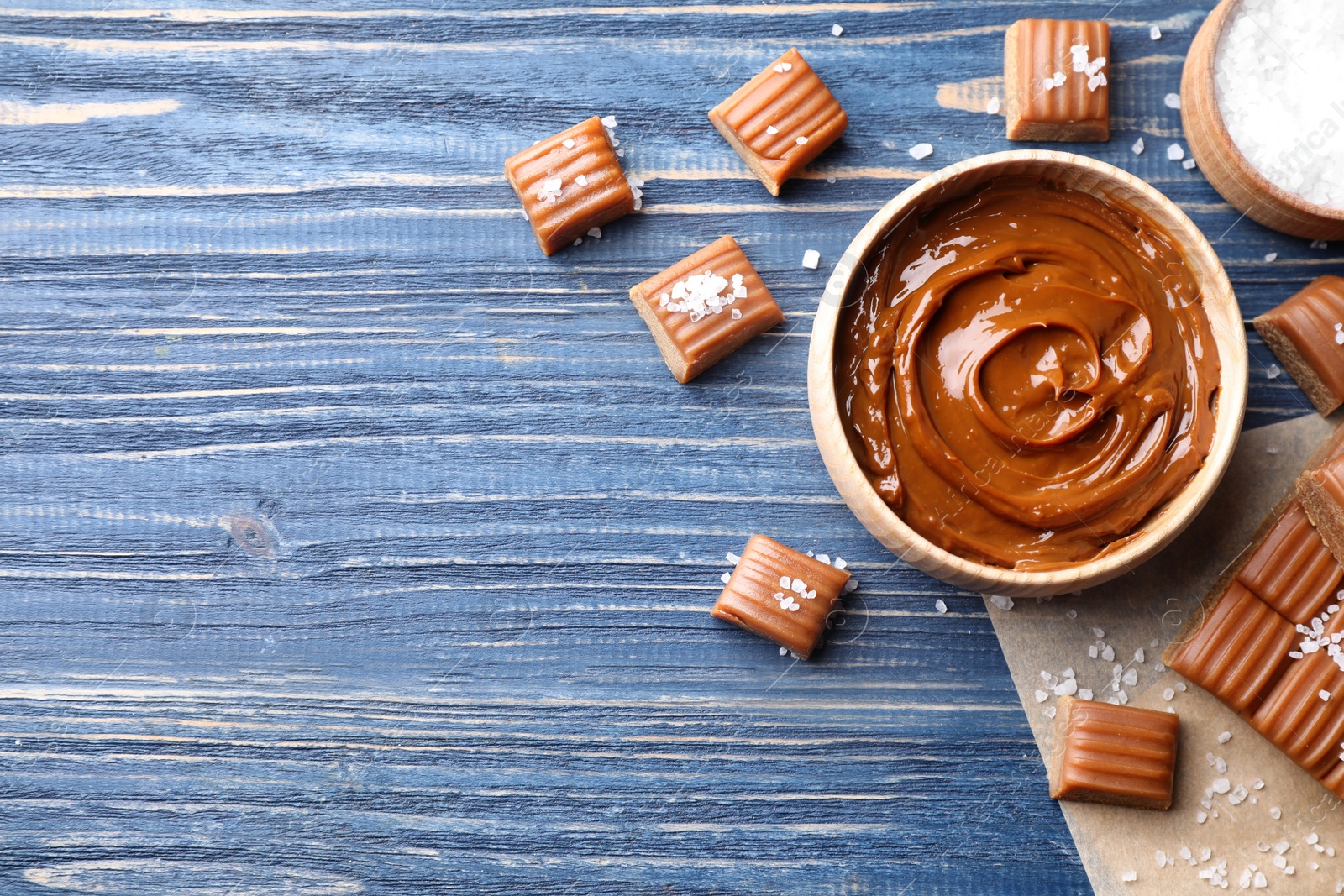 Photo of Salted caramel on blue wooden table, flat lay. Space for text