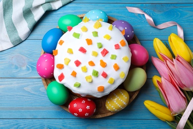 Easter cake, color eggs and tulips on blue wooden table, flat lay