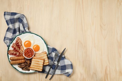 Plate of fried eggs, sausages, mushrooms, beans, bacon and toasts on wooden table, flat lay with space for text. Traditional English breakfast
