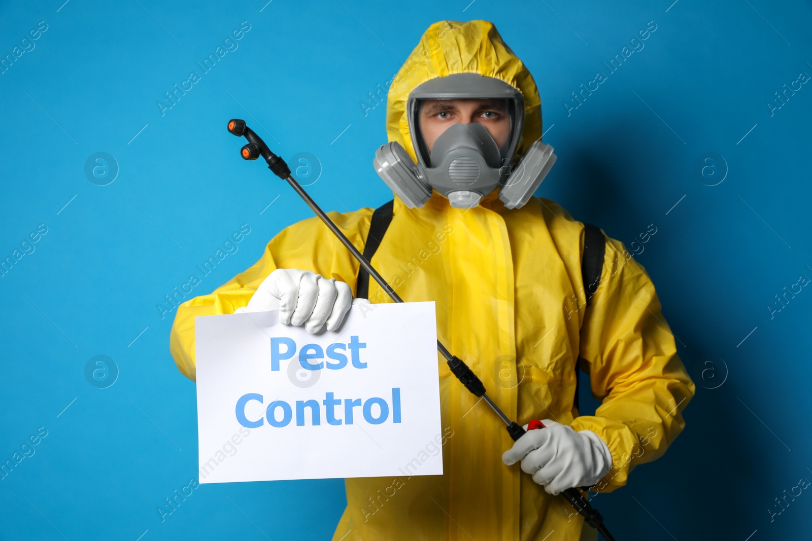 Photo of Man wearing protective suit with insecticide sprayer holding sign PEST CONTROL on blue background