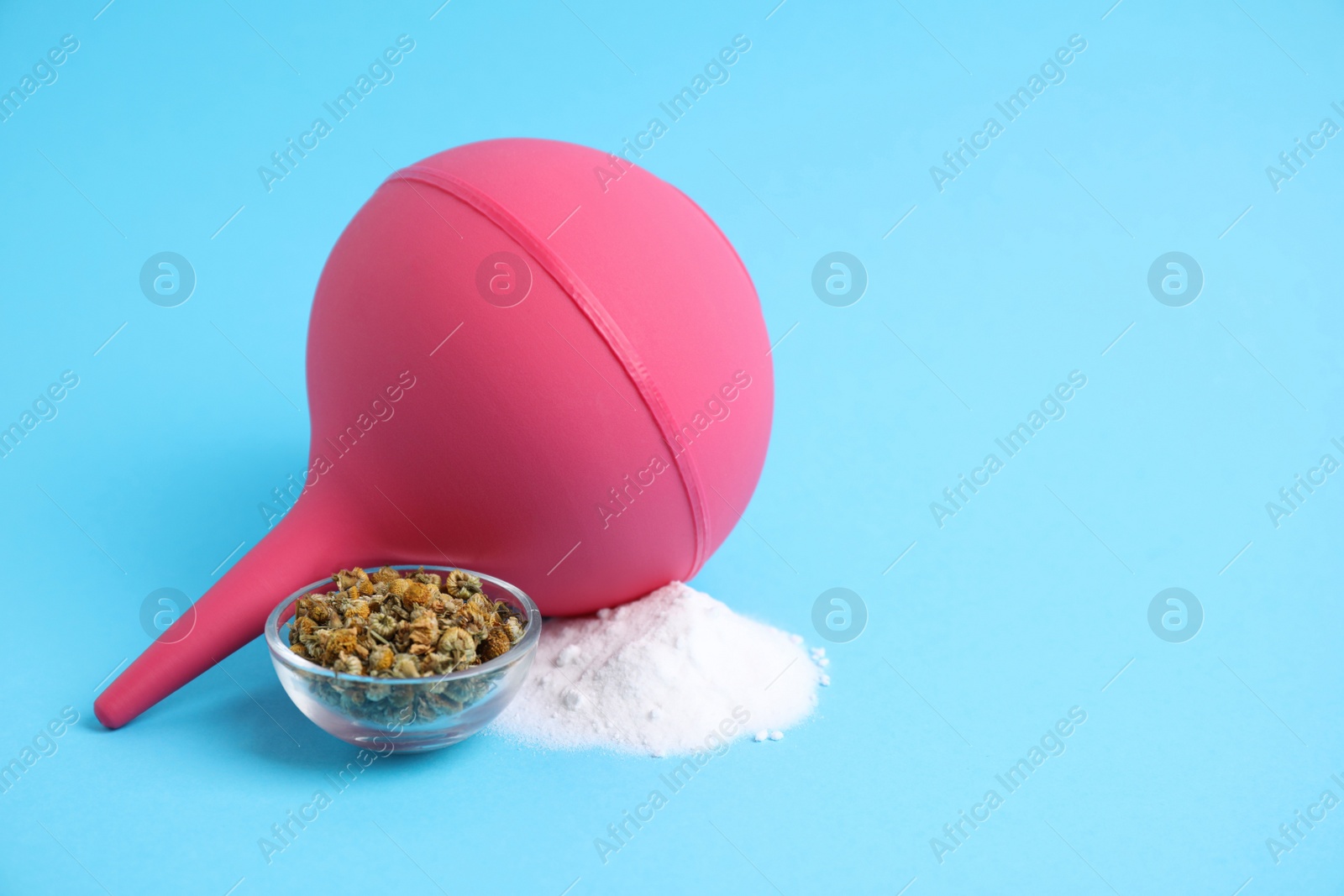 Photo of Pink enema, soda powder and dry chamomile flowers on light blue background. Space for text