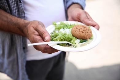 Photo of Poor man with donated food on plate outdoors, closeup