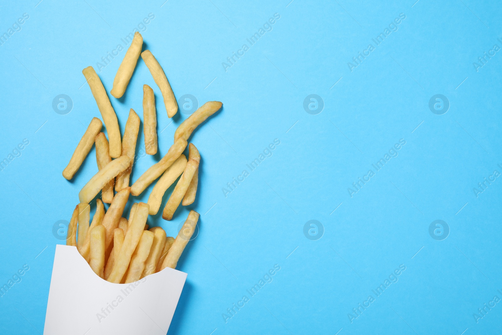 Photo of Paper cup with French fries on light blue table, flat lay. Space for text