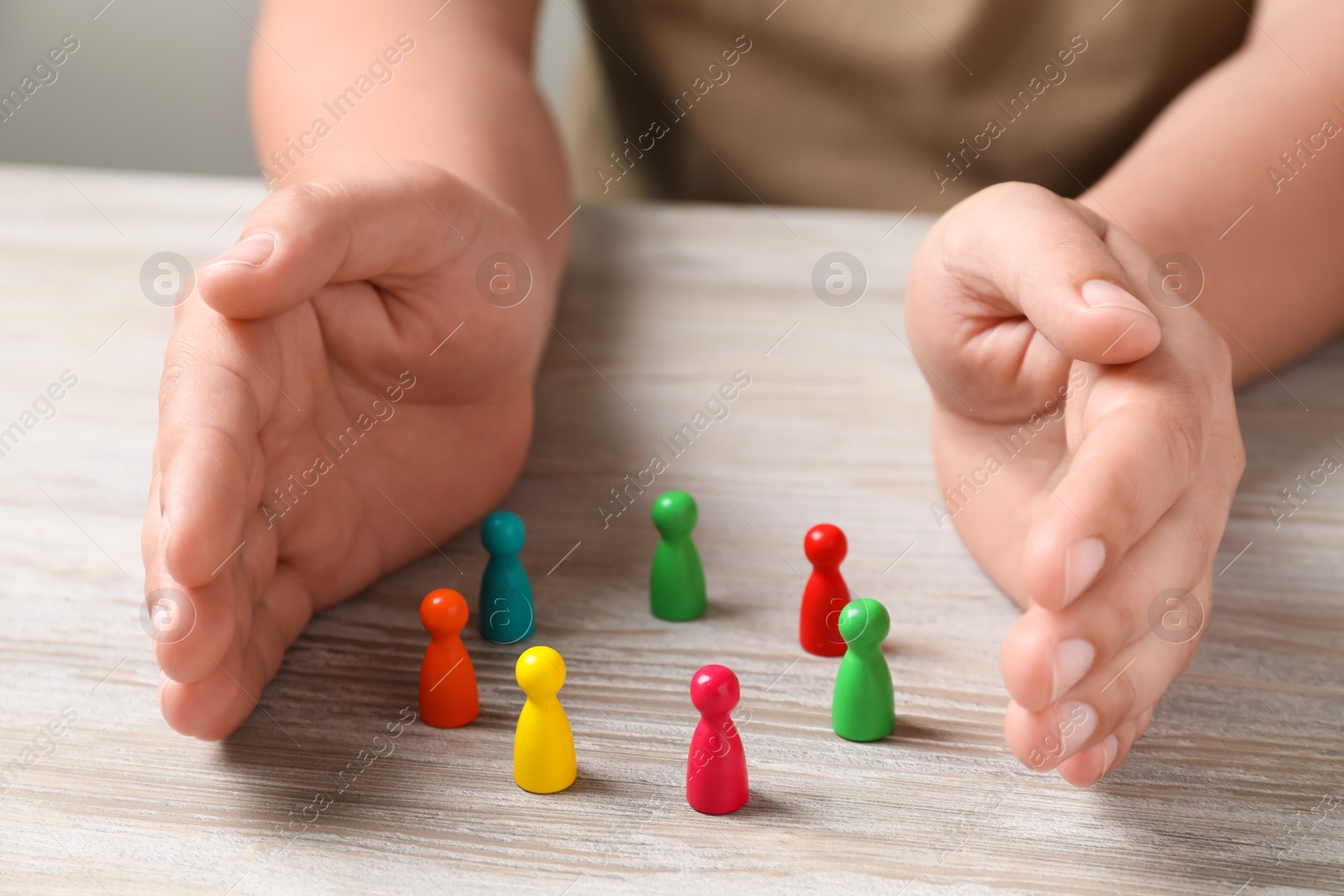 Photo of Woman protecting colorful pawns at white wooden table, closeup. Social inclusion concept