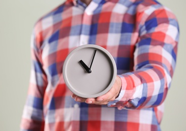 Young man holding alarm clock on grey background. Time concept