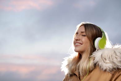 Photo of Young woman with headphones listening to music outdoors, space for text