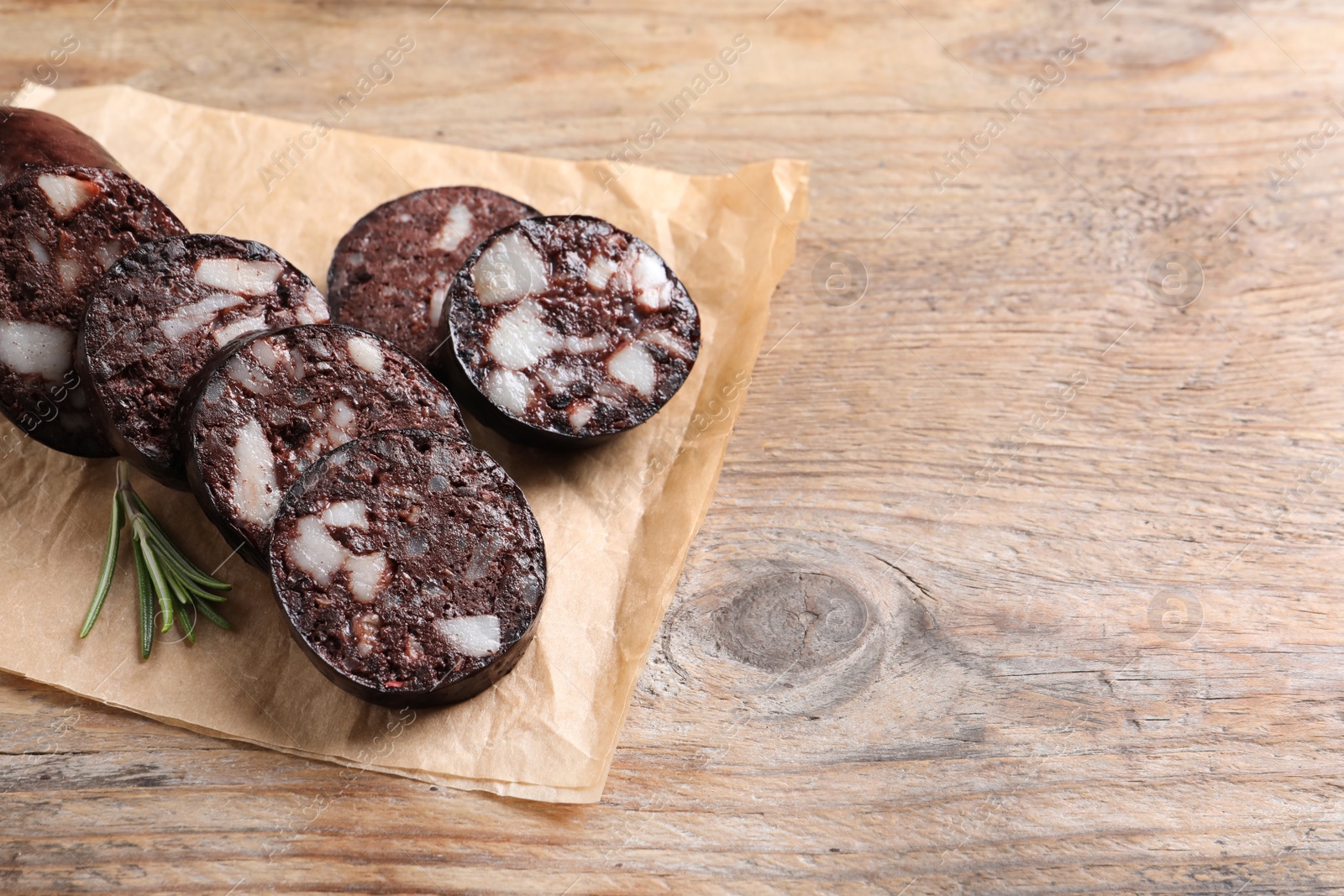 Photo of Slices of tasty blood sausage with rosemary on wooden table, space for text