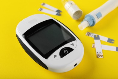 Digital glucometer, lancet pen and test strips on yellow background. Diabetes control