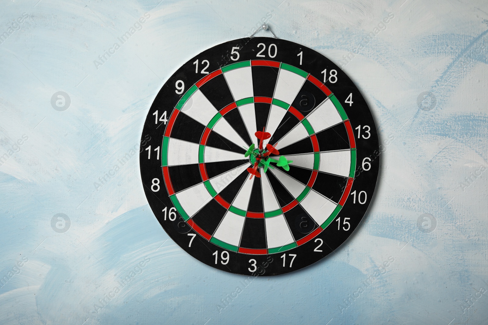 Photo of Dart board with arrows hitting target on light blue wall