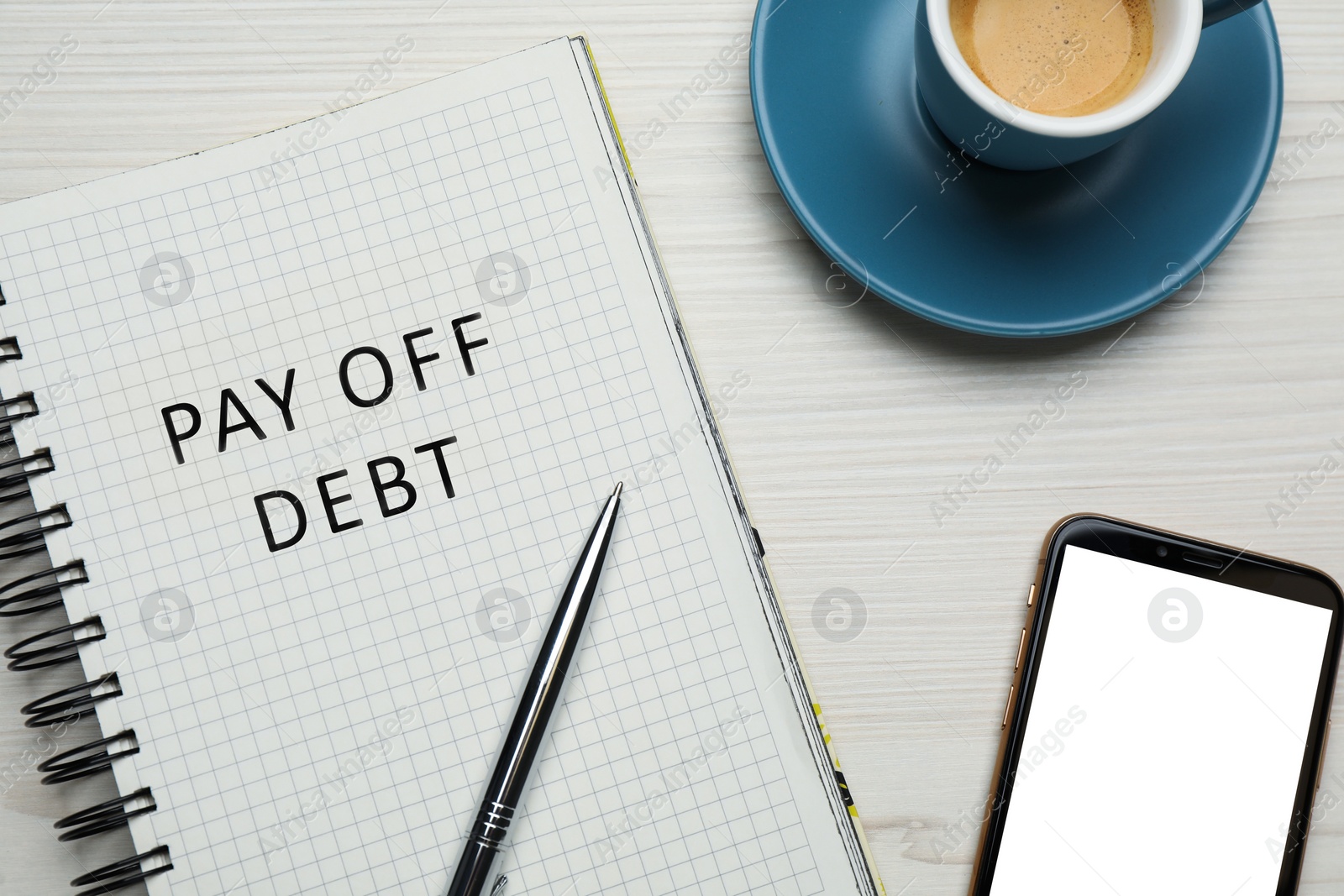 Image of Notebook with phrase Pay Off Debt, cup of coffee, smartphone and pen on white wooden table, flat lay