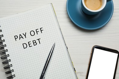 Notebook with phrase Pay Off Debt, cup of coffee, smartphone and pen on white wooden table, flat lay