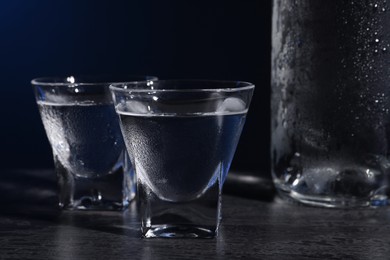 Photo of Vodka in shot glasses on black table against dark background, closeup