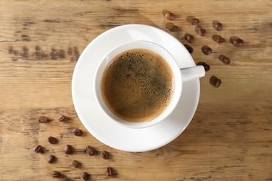 Cup of tasty coffee and beans on wooden table, flat lay