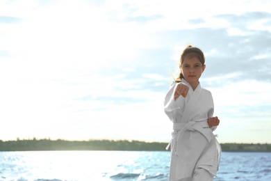 Cute little girl in kimono practicing karate near river