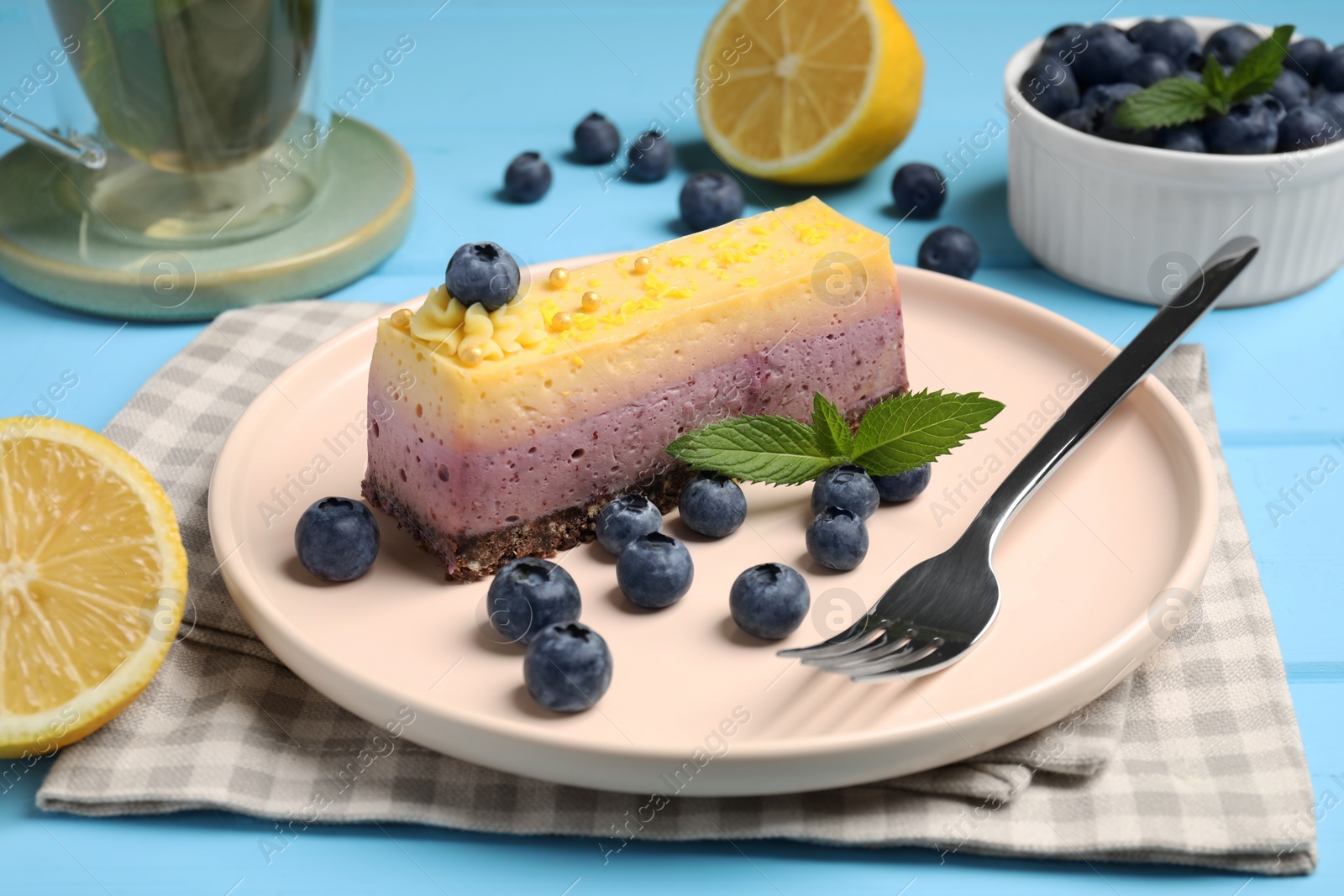 Photo of Delicious cheesecake with blueberry, lemon and mint on light blue wooden table