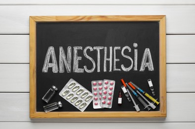 Photo of Blackboard with word Anesthesia, syringes and drugs on white wooden table, top view