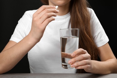 Woman holding pill and glass of water at table, closeup