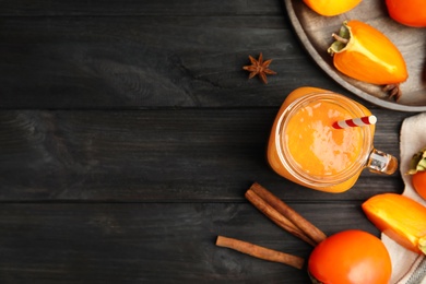 Photo of Tasty persimmon smoothie with straw on black wooden table, flat lay. Space for text