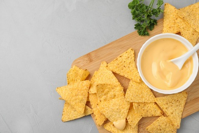 Board with Mexican nacho chips and sauce on grey table, top view. Space for text