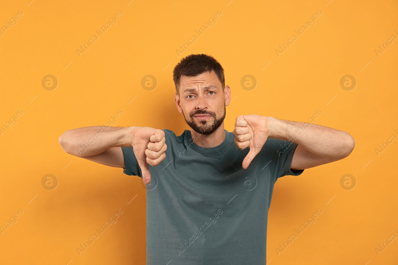 Photo of Man showing thumbs down on orange background