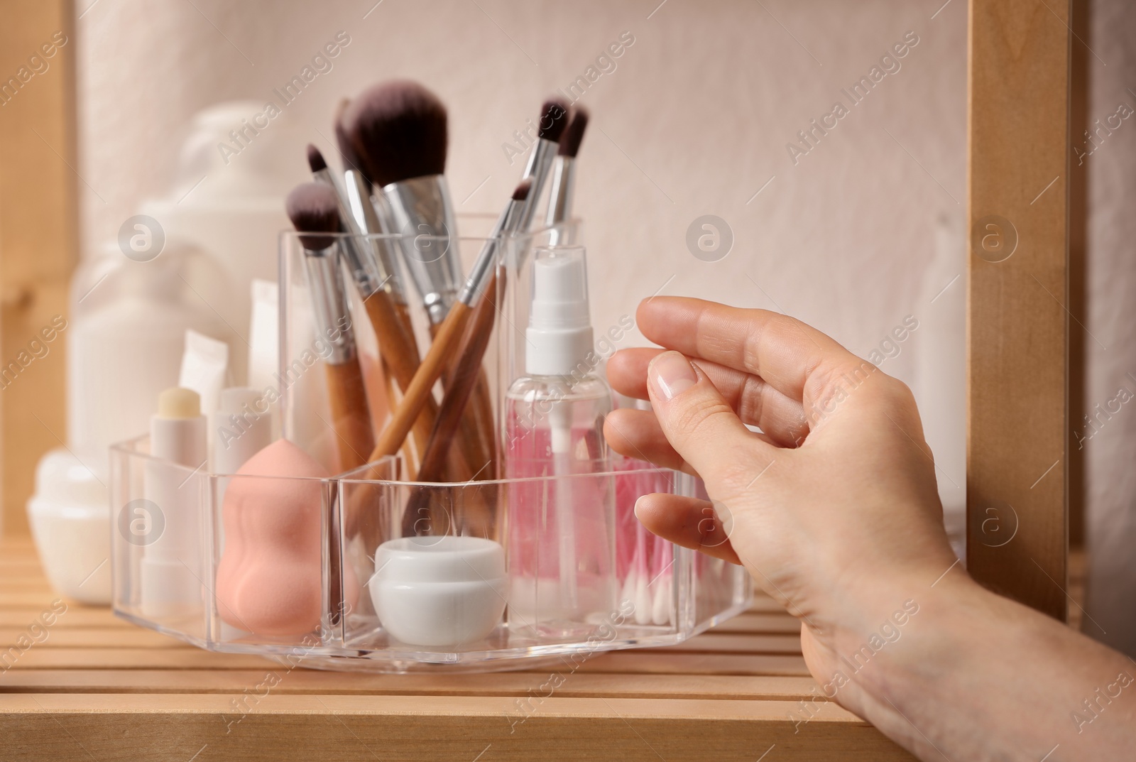 Photo of Woman taking cosmetic products from holder on shelf