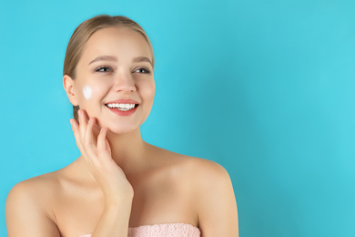 Young woman washing face with cleansing foam on light blue background, space for text. Cosmetic product