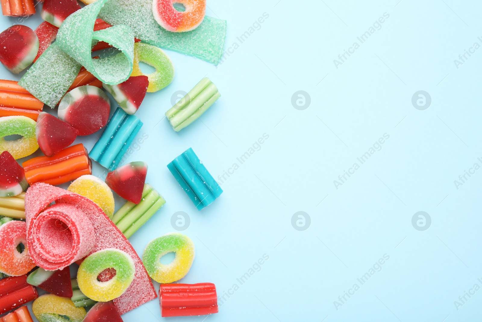 Photo of Many different jelly candies on light blue background, flat lay. Space for text