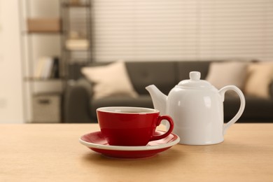 Photo of Red cup of fresh tea and teapot on wooden table in room