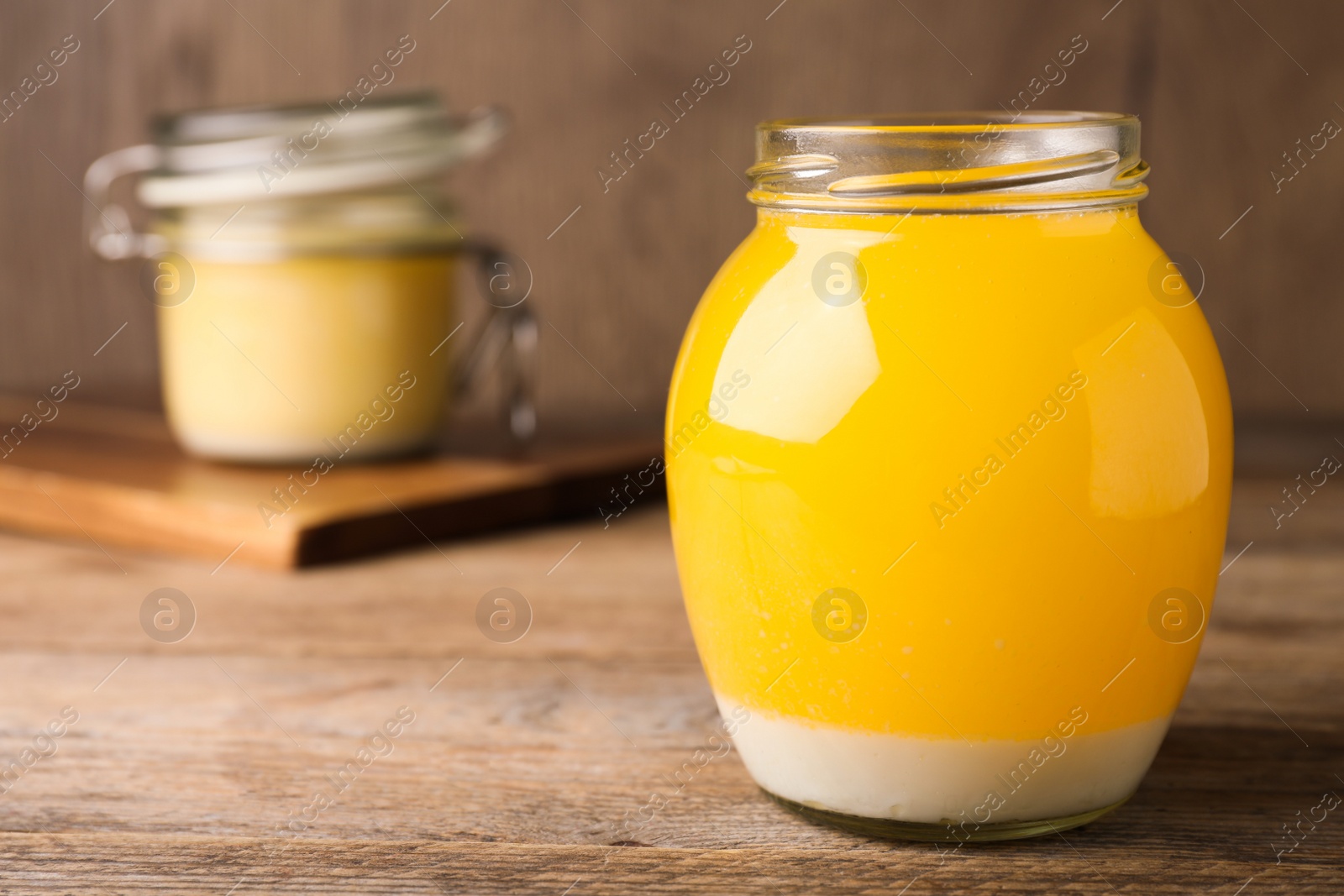 Photo of Glass jar of Ghee butter on wooden table, closeup. Space for text