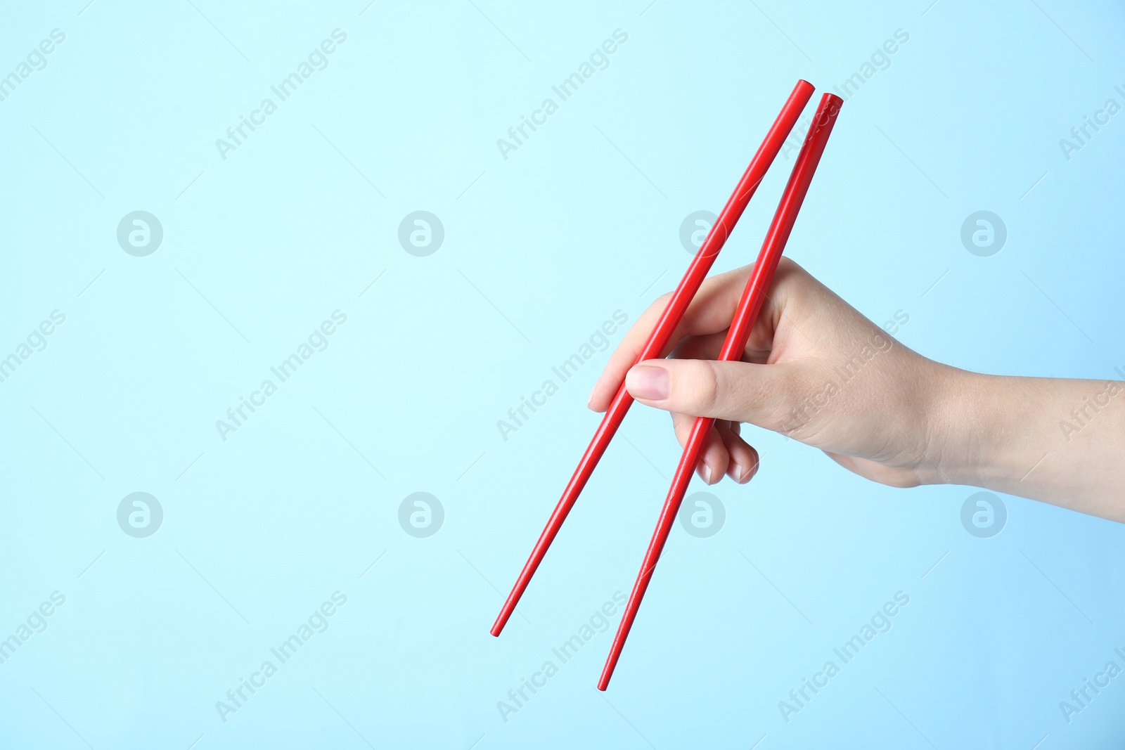 Photo of Woman holding pair of red chopsticks on light blue background, closeup. Space for text