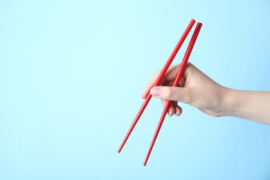 Woman holding pair of red chopsticks on light blue background, closeup. Space for text