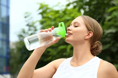 Young woman drinking water outdoors. Refreshing drink